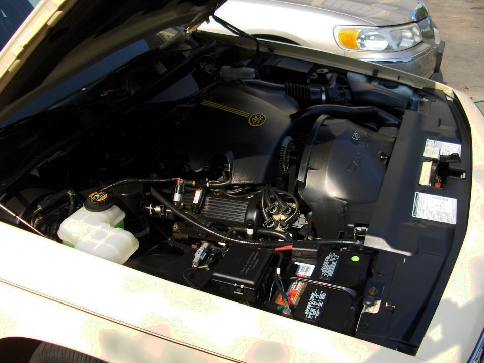 Open engine bay of a white car with black engine cover and battery