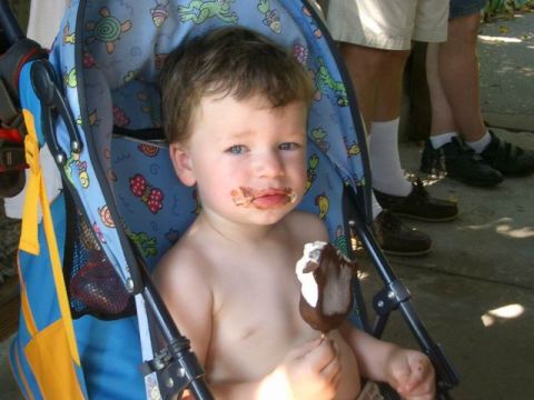 1995 Ford Bronco - A young child sits in a stroller, with chocolate smeared around their mouth and holding an ice cream bar.