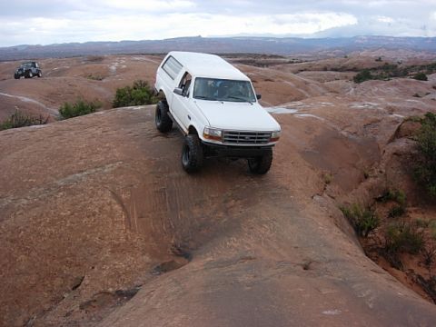 1993 Ford Bronco - White 1995 Ford Bronco navigates a rocky trail in Moab, with another vehicle visible in the distance.