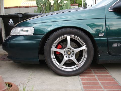 1993 Ford Taurus - Close-up of a green sedan's front wheel and fender, showing custom rims and brake calipers.