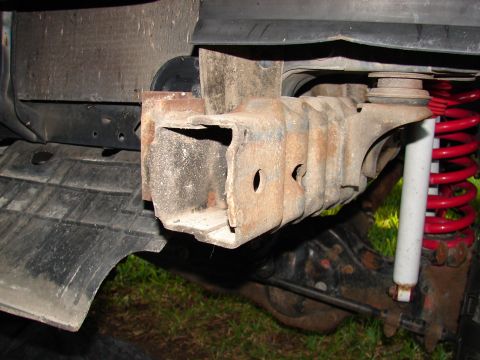 1996 Ford Bronco - Close-up of a corroded tow hook mount, showing suspension components and part of the tire well.