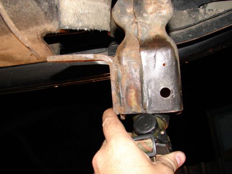 1996 Ford Bronco - A hand holds a tool near a rusty tow hook bracket, with a dark background.