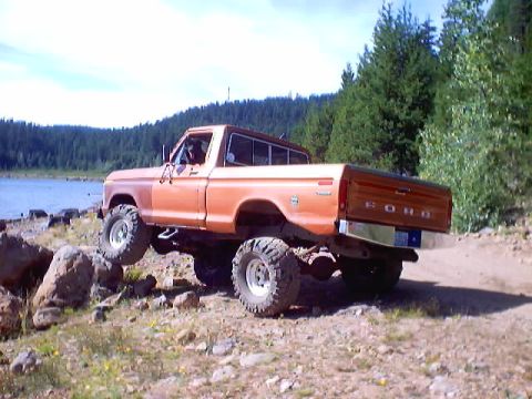 1976 Ford F-100 - Orange lifted Ford short-bed 4x4 pickup with a white roof, FORD-stamped tailgate and tall mud-terrain tires on white wheels, parked at an a…