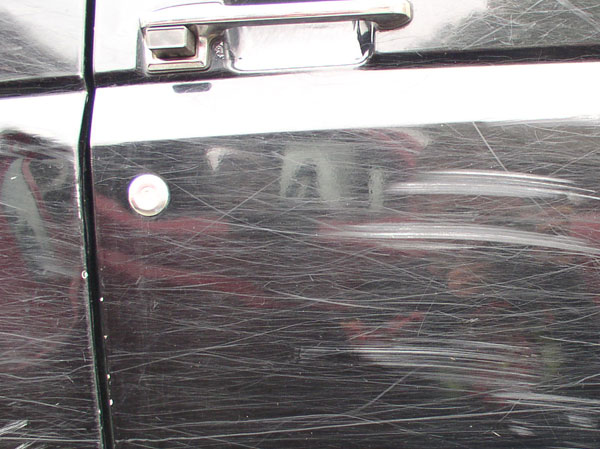 Close-up of a scratched dark vehicle door panel and chrome handle