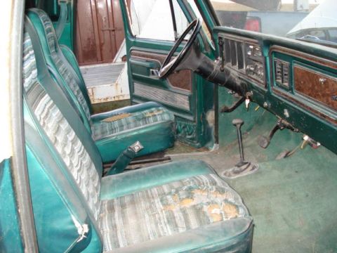 1979 Ford Bronco - The interior of a vintage truck shows faded green upholstery and a wood-grain dashboard.