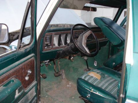 1979 Ford Bronco - The interior of this 1979 Ford Bronco shows its dashboard, steering wheel, and a torn green striped driver's seat.