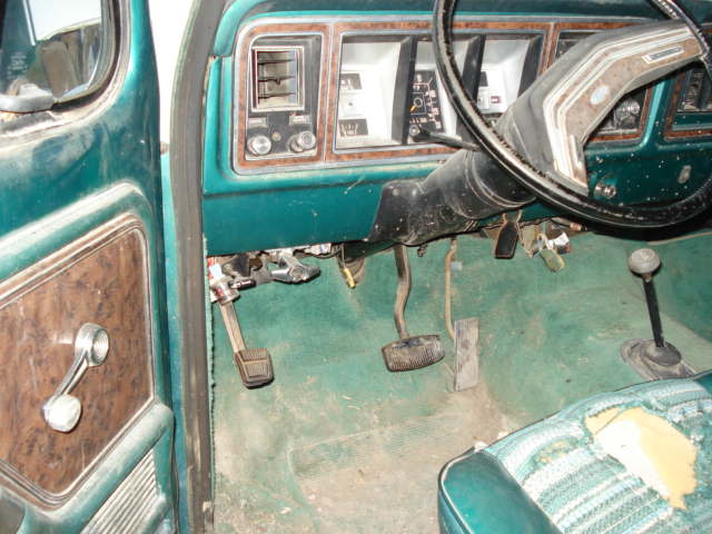 Green interior of a 1978 Ford Bronco with wood-grain door panel, pedals, steering wheel, and dashboard visible