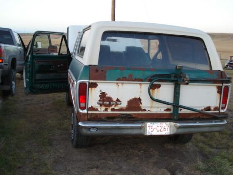 1979 Ford Bronco - This heavily rusted Ford Bronco is parked outdoors next to another vehicle, with its rear facing the camera.