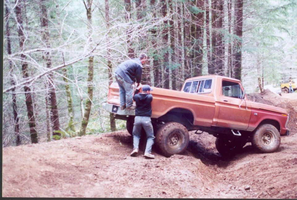 Lifted orange 1970s Ford F-series 4x4 pickup on a muddy forest trail