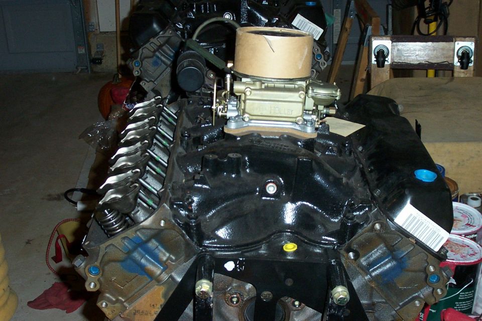 Black-painted V8 engine on a stand with gold Holley four-barrel carburetor and valve covers off