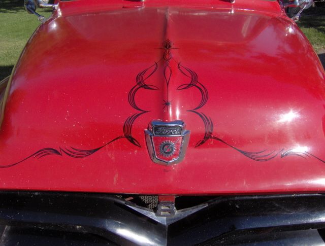 Red truck hood with black pinstriping, chrome Ford emblem, and V-8 badge above the grille