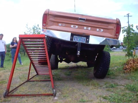 1976 Ford F-100 - Rear view of an orange 1970s Ford pickup on grass with one rear wheel climbed onto a red steel RTI flex ramp, twisting the rear axle and ex…