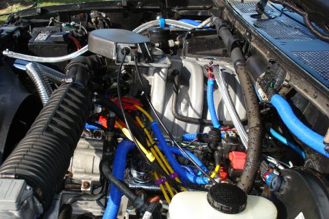 1994 Ford Bronco - Engine bay with numerous blue and yellow hoses, a large black air intake, and a Supermotors.net watermark.