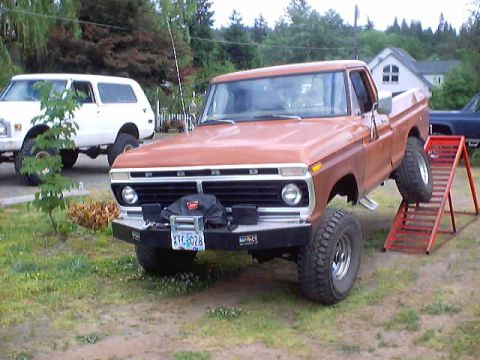 1976 Ford F-100 - This 1976 Ford F-100 pickup truck features a custom front bumper and large off-road tires, with a white SUV visible in the background.