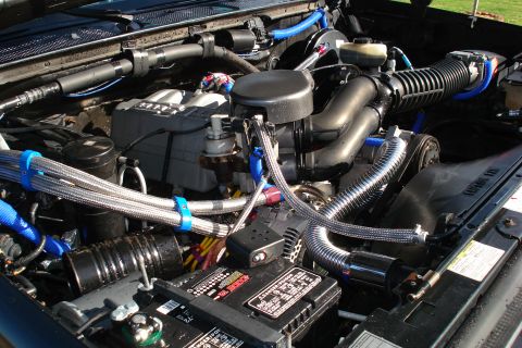 1994 Ford Bronco - Close-up view of a modified engine bay, chrome braided hoses and blue fluid lines.