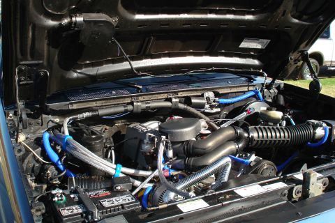 1994 Ford Bronco - The engine bay of a vehicle is shown with various components and blue hoses.
