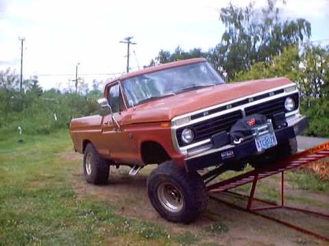1976 Ford F-100 - A lifted orange pickup truck is positioned on a set of red ramps outdoors.