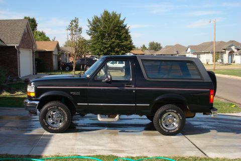 1994 Ford Bronco - Side view of a black 1994 Ford Bronco parked on a concrete driveway with houses in the background.