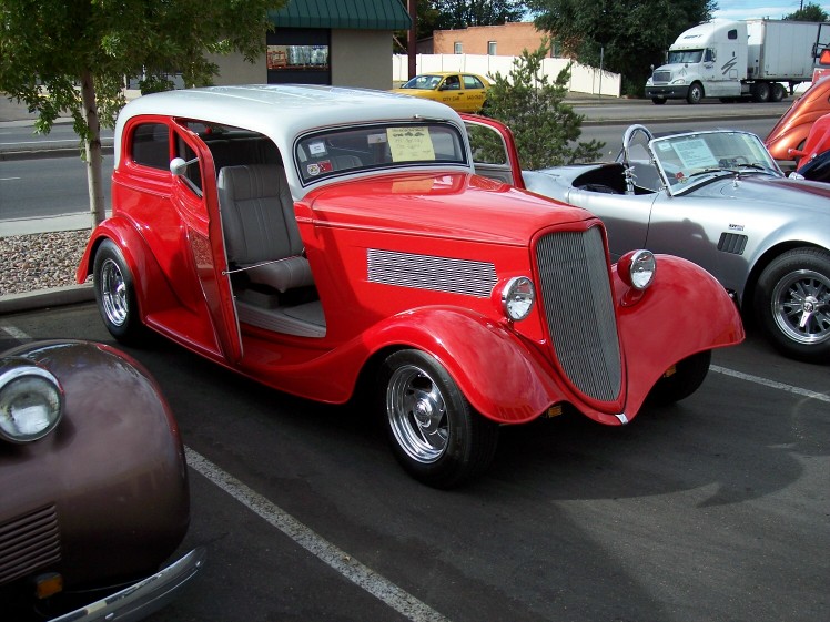 Red hot rod sedan with white roof and doors open, parked next to a silver convertible