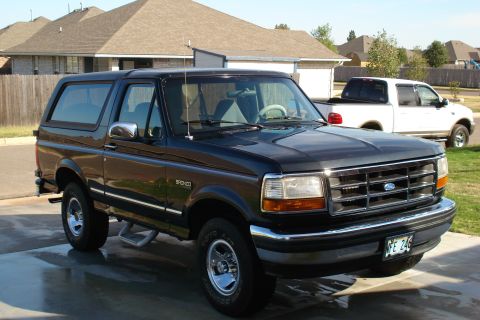 1994 Ford Bronco - A black 1994 Ford Bronco is parked in a driveway with a white pickup truck in the background.