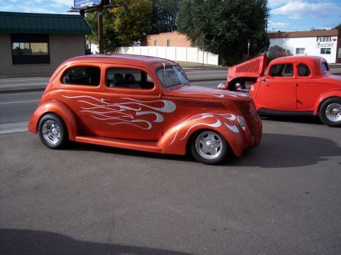 1972 Ford Ranchero - An orange hot rod with silver flame decals is parked next to a red coupe.