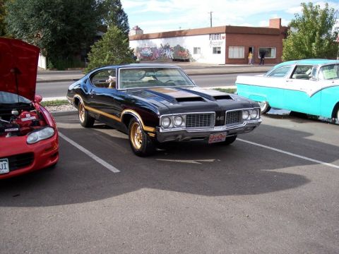 1972 Ford Ranchero - A black 1970 Oldsmobile 442 with gold accents is parked next to a red car and a turquoise and white classic car.