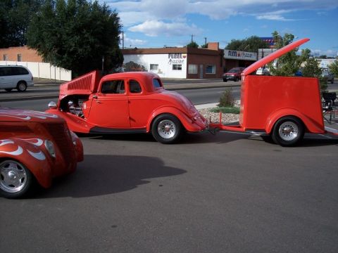 1972 Ford Ranchero - Two hot rod coupes, one towing a trailer, parked on a street with buildings in the background.