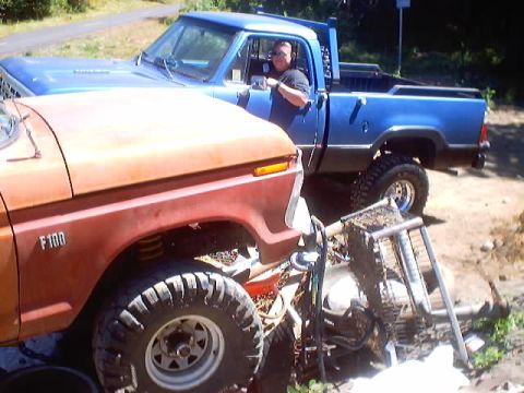 1976 Ford F-100 - Orange 1976 Ford F-100 fender and wheel are visible next to a blue pickup truck with a driver.