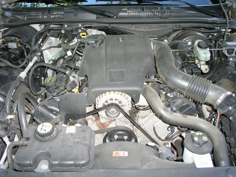 Engine bay showing black engine cover, serpentine belt, alternator and air intake tube.