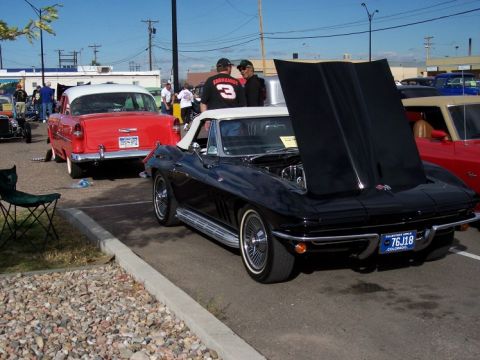 1972 Ford Ranchero - A black 1965 Corvette convertible is parked with its hood open at a car show, next to a red classic car.