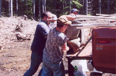 1976 Ford F-100 - People are loading large rocks into the bed of a red truck in a wooded area.
