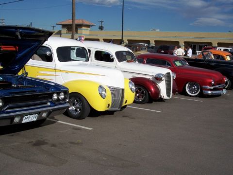 1972 Ford Ranchero - A row of classic cars, including a white and yellow panel van and a blue muscle car, are parked in a lot.