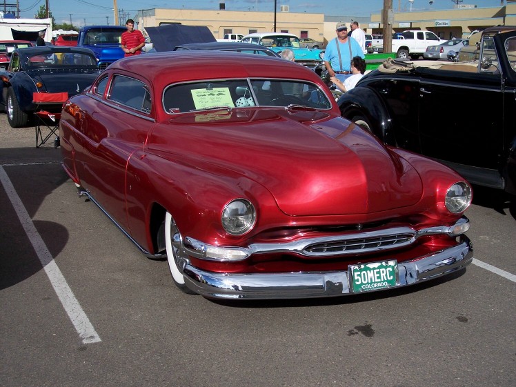 Red custom coupe with wide whitewall tires and chrome grille. License plate reads 50MERC COLORADO