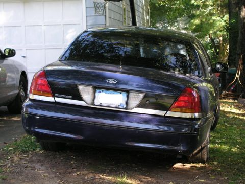 1999 Ford Crown Victoria - The rear of a dark blue 2003 Ford Crown Victoria is visible, parked in a driveway.