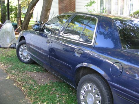 1999 Ford Crown Victoria - A blue 1999 Ford Crown Victoria is parked on a grassy area next to a driveway.