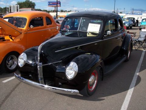 1972 Ford Ranchero - A black 1940 coupe is parked at a car show with an orange coupe beside it.