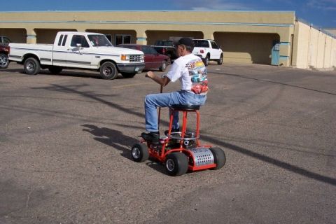 1972 Ford Ranchero - A person rides a custom-built rolling stool in a parking lot with several vehicles.