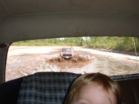 1989 Ford Bronco - A red SUV navigates a muddy path, kicking up water and dirt.