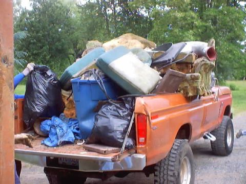 1976 Ford F-100 - A 1976 Ford F-100 pickup truck is filled with garbage bags and old furniture, ready for disposal.