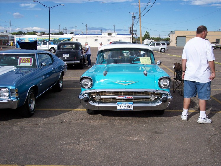 Turquoise 1957 Chevrolet Bel Air with white roof and chrome grille, parked next to a blue muscle car. License plate 128-HYU
