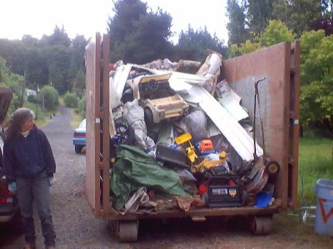 1976 Ford F-100 - A dumpster is filled with various debris, including toys and what appear to be car parts, suggesting a cleanup or demolition site.