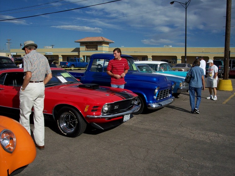Red muscle car with black stripes and chrome wheels parked at a car show