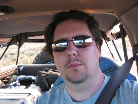 1995 Ford Bronco - A man takes a selfie while driving, with the landscape reflected in his sunglasses.