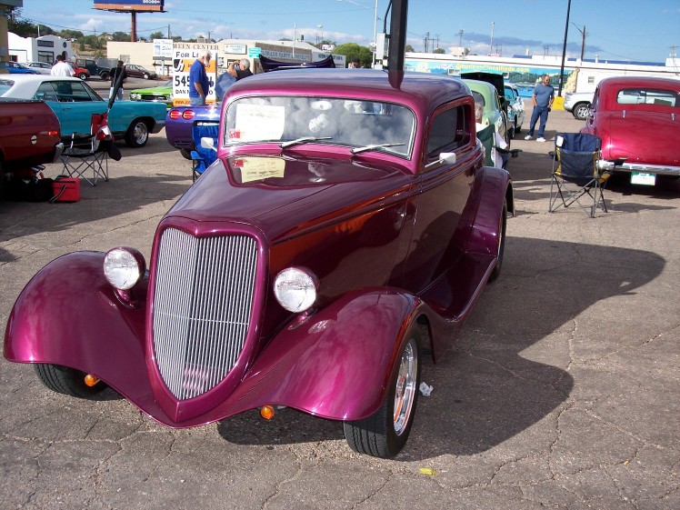Custom purple hot rod coupe with a tall grille, parked at an outdoor car show. Other vehicles visible in background