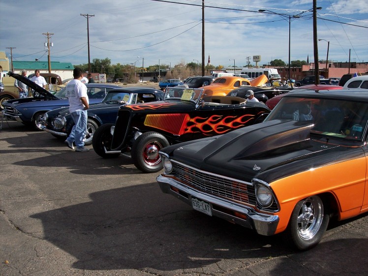 Black and orange 1966 Chevrolet Nova with a large hood scoop and flame decals parked at a car show
