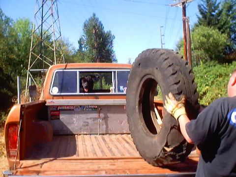 1976 Ford F-100 - Looking forward into the wood-plank bed of an orange Ford pickup where a person in a dark T-shirt and work gloves is lifting an oversized m…