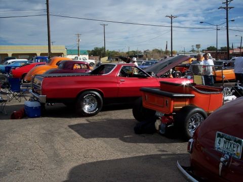 1972 Ford Ranchero - A red pickup truck and an orange hot rod are parked at an outdoor event with other vehicles and people.