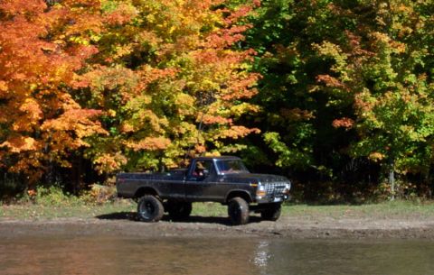 1979 Ford Bronco - A lifted black 1979 Ford F-Series pickup truck sits by the water during autumn.