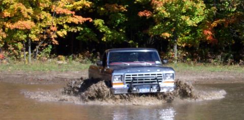1979 Ford Bronco - A Ford F-Series truck splashes through a muddy puddle with autumn trees in the background.