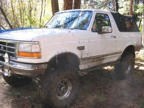 1995 Ford Bronco - Mud-covered white Ford Bronco with a soft top rear, seen off-road.